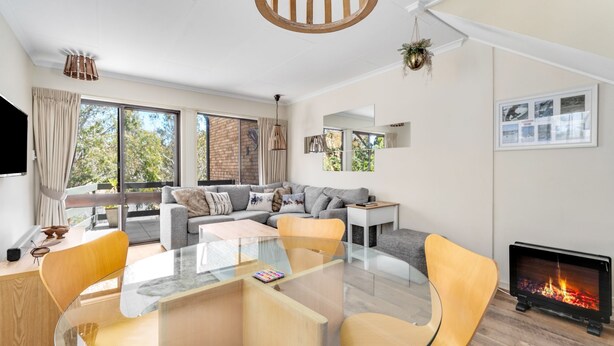 A modern living room with a glass coffee table, a fireplace, and a large window with curtains.