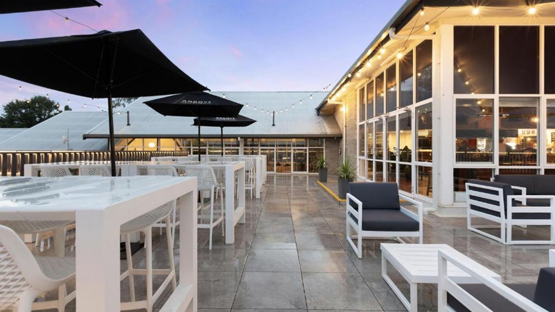 An outdoor patio with white furniture, umbrellas, and a building with large windows.