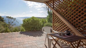 A patio with a view of the sea, a wooden table, and a white plastic chair. - Seeblick 3 - 1BR Lakefront Apartment l Central Location l Off Street Parking (JINDABYNE)