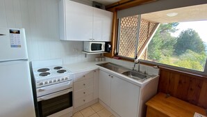 A compact kitchen with a stove, microwave, sink, and wooden cabinets. - Seeblick 3 - 1BR Lakefront Apartment l Central Location l Off Street Parking (JINDABYNE)