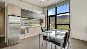 A modern kitchen with stainless steel appliances, a dining area with a glass table, and large windows offering a view of the outdoors. - Ecocrackenback 7 'Sustainable chalet close to the slopes.' (Crackenback)