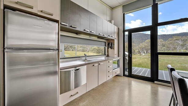 A modern kitchen with stainless steel appliances, a large window, and a view of a grassy landscape. - Ecocrackenback 7 'Sustainable chalet close to the slopes.' (Crackenback)