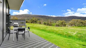 A patio with a grill and chairs, overlooking a grassy field and hills. - Ecocrackenback 7 'Sustainable chalet close to the slopes.' (Crackenback)