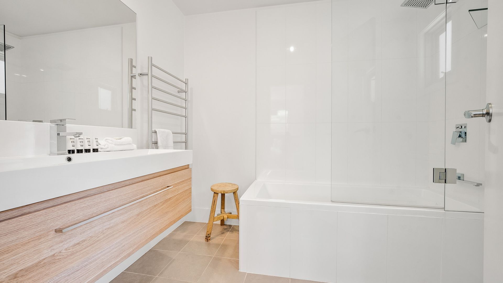Une salle de bain moderne avec un meuble-lavabo blanc, un tabouret en bois, une cabine de douche en verre et une baignoire.