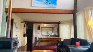 A cozy living room with a fireplace, a dining area, and a kitchen visible through an open door. - Snowgums on the Lake - Charming 4BR Home l Amazing Lake Views l Balcony (EAST JINDABYNE)