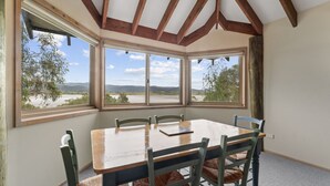Ein Essbereich mit großem Tisch und Stühlen, großen Fenstern mit Blick auf einen Fluss und Hügel sowie Holzbalken an der Decke.