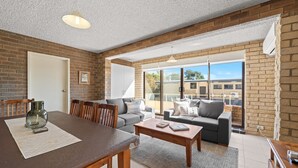 A spacious living area with a dining table, sofas, and a large sliding glass door leading to a balcony. - Central Park 4 - 3BR Ground Floor Apartment l Central Location (Jindabyne)