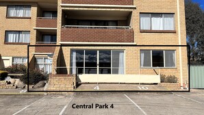 A multi-story brick building with a balcony on the second floor, large windows, and a parking area labeled "Central Park 4". - Central Park 4 - 3BR Ground Floor Apartment l Central Location (Jindabyne)