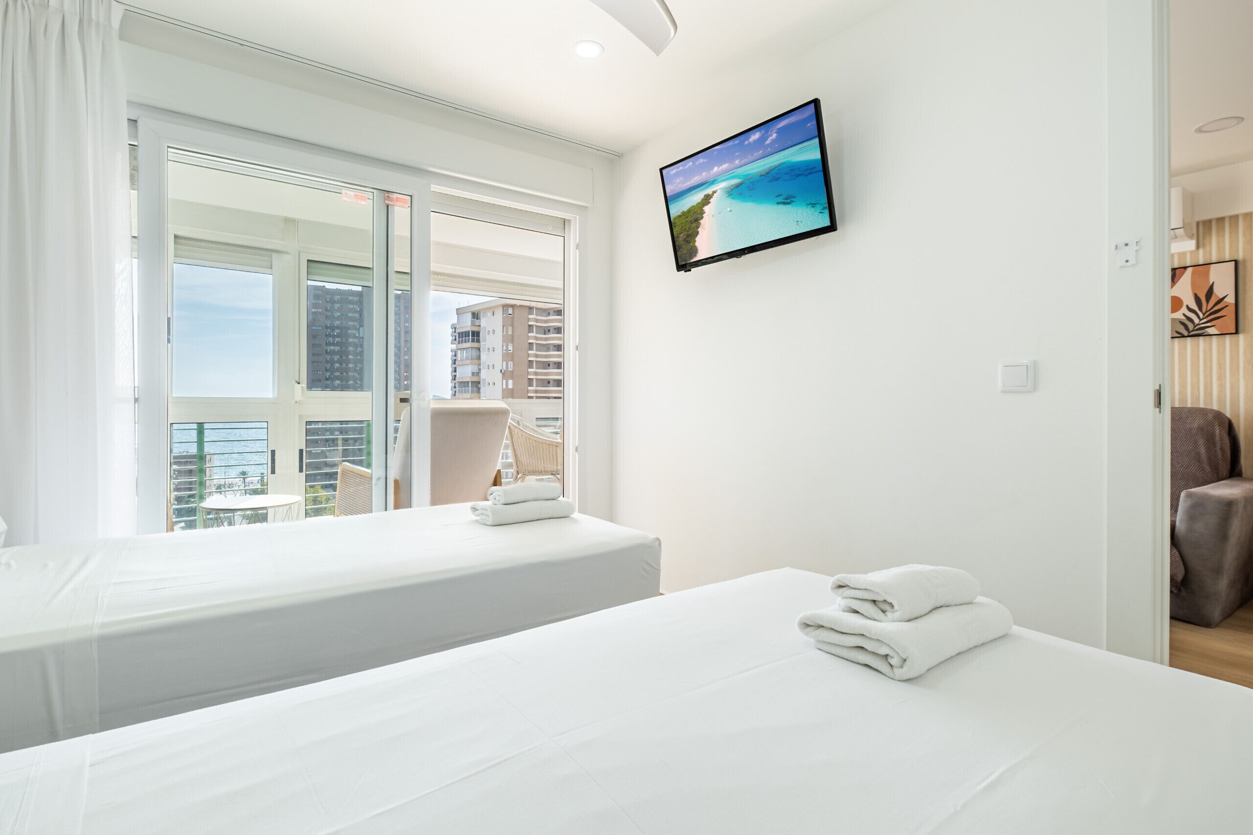 Camera d'albergo con due letti, un'ampia finestra vista edifici e una televisione a schermo piatto appesa al muro.