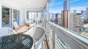 A balcony with wicker chairs and a glass table, overlooking a cityscape with tall buildings. - Niza 11-A (Benidorm)