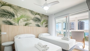 A hotel room with two beds, a ceiling fan, a large window with a view of buildings, and a balcony with a chair. - Niza 11-A (Benidorm)