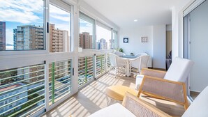 A modern apartment with large windows, a balcony, wicker furniture, and a city view. - Niza 11-A (Benidorm)