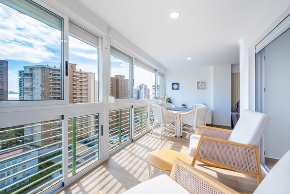 A modern apartment with large windows, a balcony, wicker furniture, and a city view.