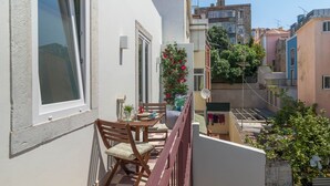 A balcony with a table and chairs, a potted plant, and a view of neighboring buildings. - Cardal Deluxe Apartment (Lisboa ciudad)