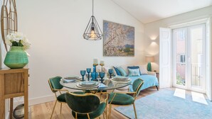 A dining area with a round glass table, green upholstered chairs, and a vase with flowers. - Cardal Deluxe Apartment (Lisboa ciudad)