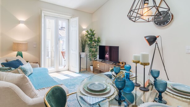 A modern living room with a glass dining table set for four, a sofa, a TV, and a potted plant. - Cardal Deluxe Apartment (Lisboa ciudad)