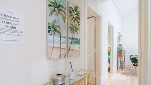A hallway with a glass console table, a painting of palm trees, and a sign with emergency contact information. - Cardal Deluxe Apartment (Lisboa ciudad)