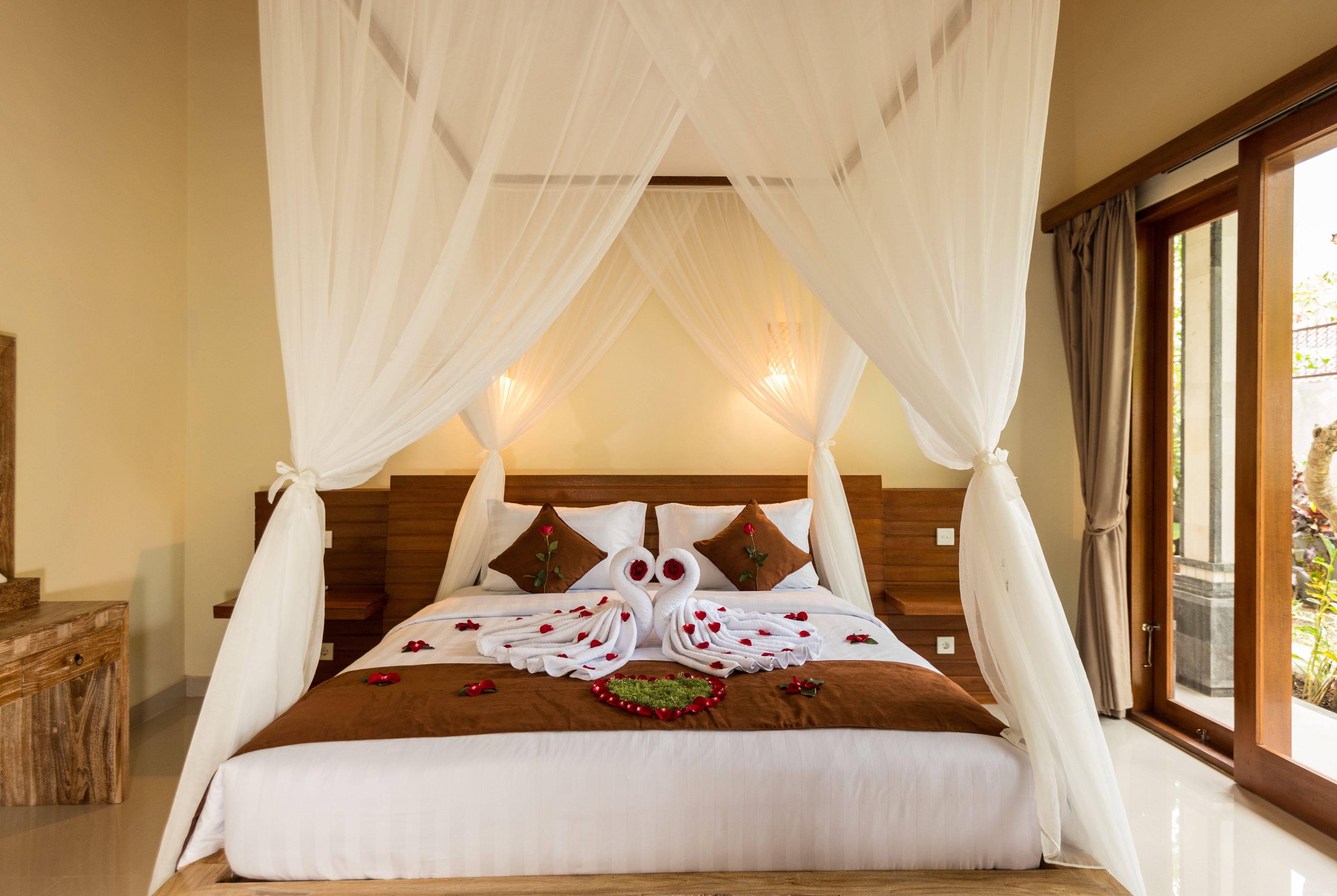 A bedroom with a canopy bed, a wooden headboard, and a view of the outdoors.