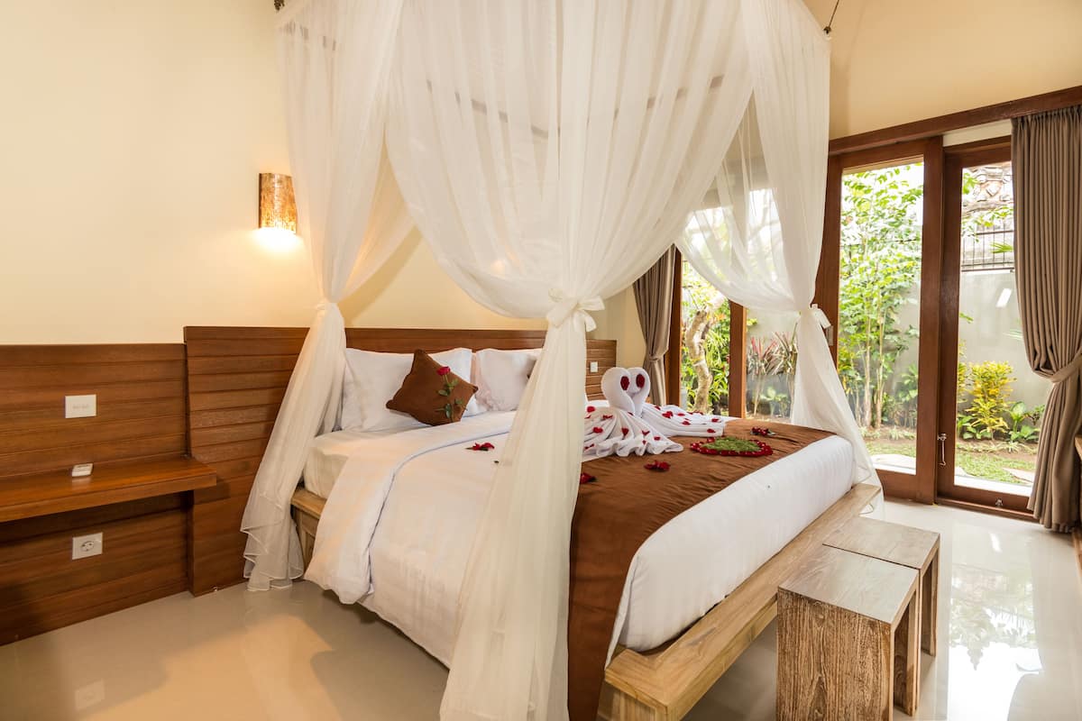 Ein Schlafzimmer mit Himmelsbett, Holz-Kopfschild, Nachttischen und Blick auf Grünfläche.
