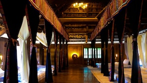 Un couloir d’hôtel avec des lits disposés le long des murs, un plancher en bois et un luminaire central.