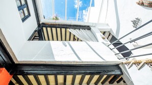 Una escalera con barandilla negra, paredes blancas y un pequeño ventanal con maceta de flores.