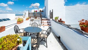 Una terraza en la azotea con una mesa redonda y sillas, plantas en macetas y vistas al mar.