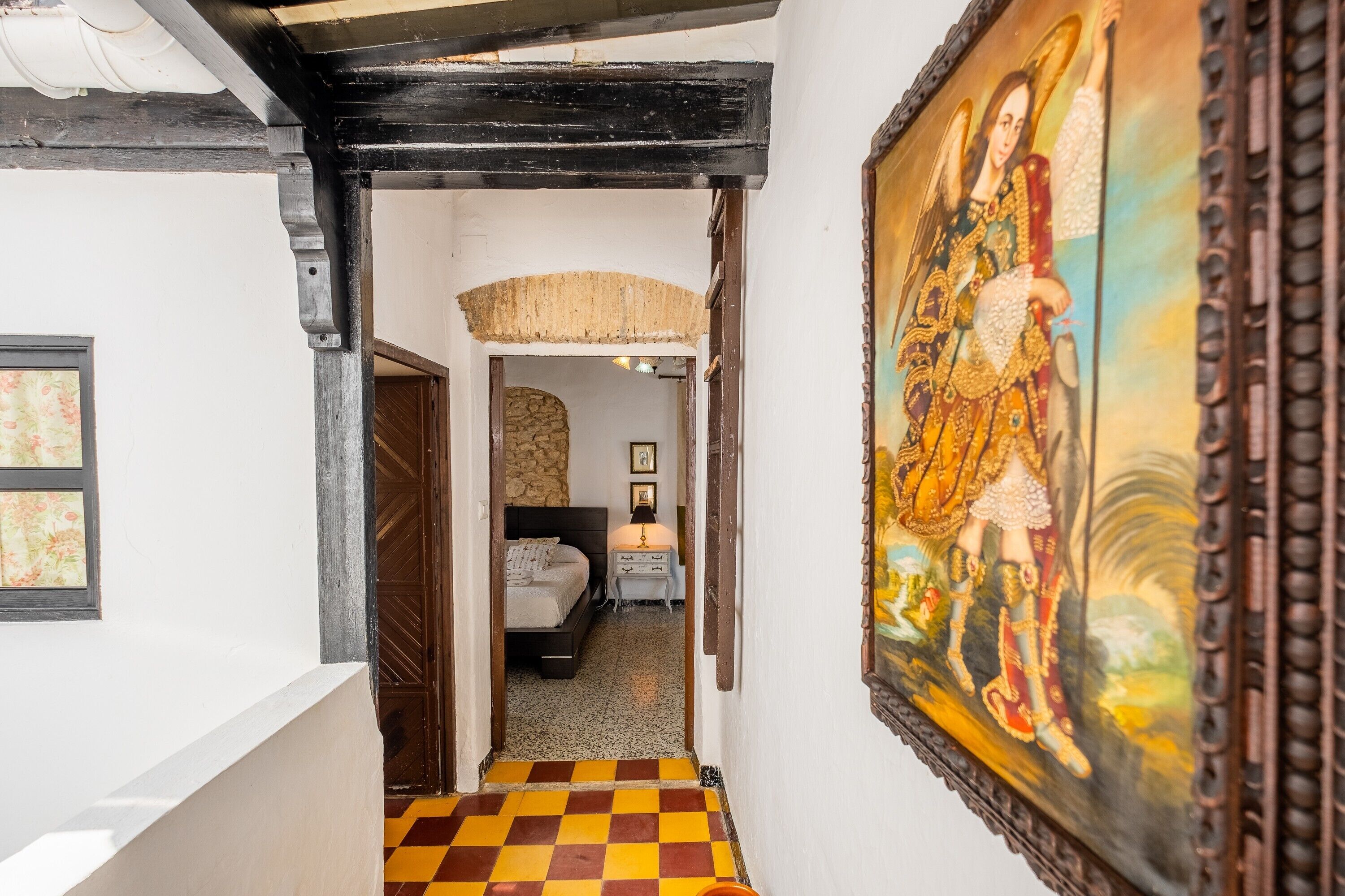 A hallway with a checkered floor, a bed with a nightstand, and a painting on the wall.