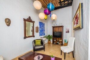 Una sala de estar con un sofá, una silla, un televisor, una mesa con un control remoto y una planta.