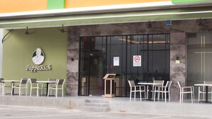Restaurante com mesas ao ar livre, toldo verde e placa com a inscrição "PappaRich".