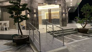Entrada de hotel com design moderno, com uma mesa de recepção, escada e plantas em vasos.