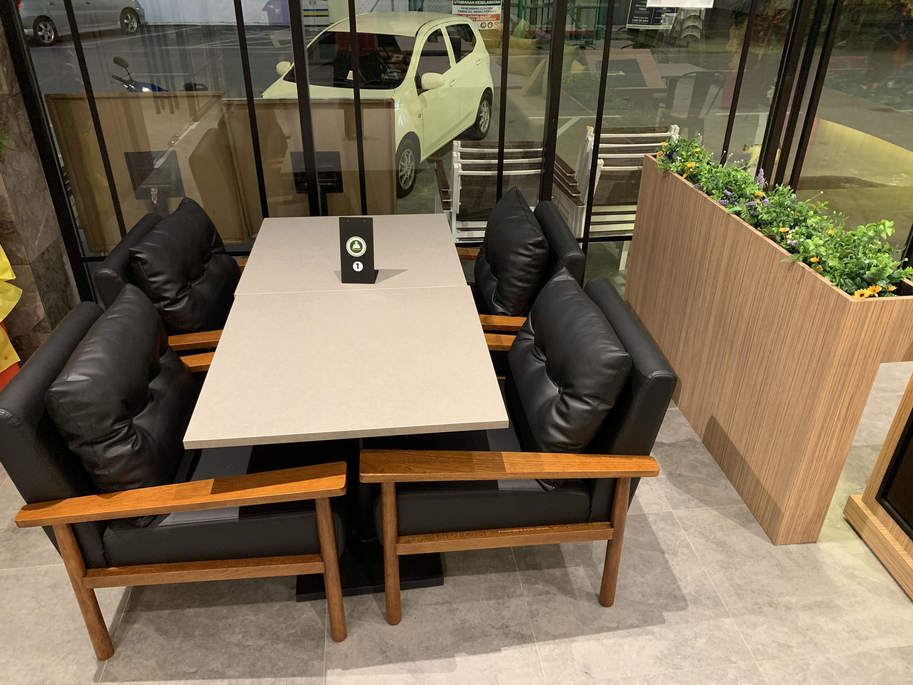 A modern seating area with a table and chairs, a small plant, and a view of the street through glass doors.