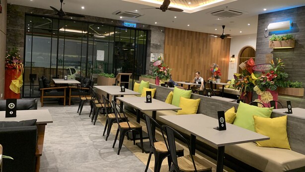 Um restaurante moderno com mesas compridas e cabines, ventiladores de teto e plantas decorativas.