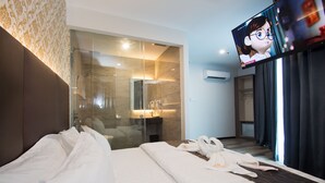 Quarto de hotel com uma cama grande, chuveiro em cabine de vidro, TV de tela plana e vista para o exterior pela janela.