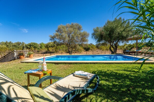 A swimming pool with lounge chairs and a table with a bottle and glass. - Mallorcan finca Ses Planes with pool (Buger)