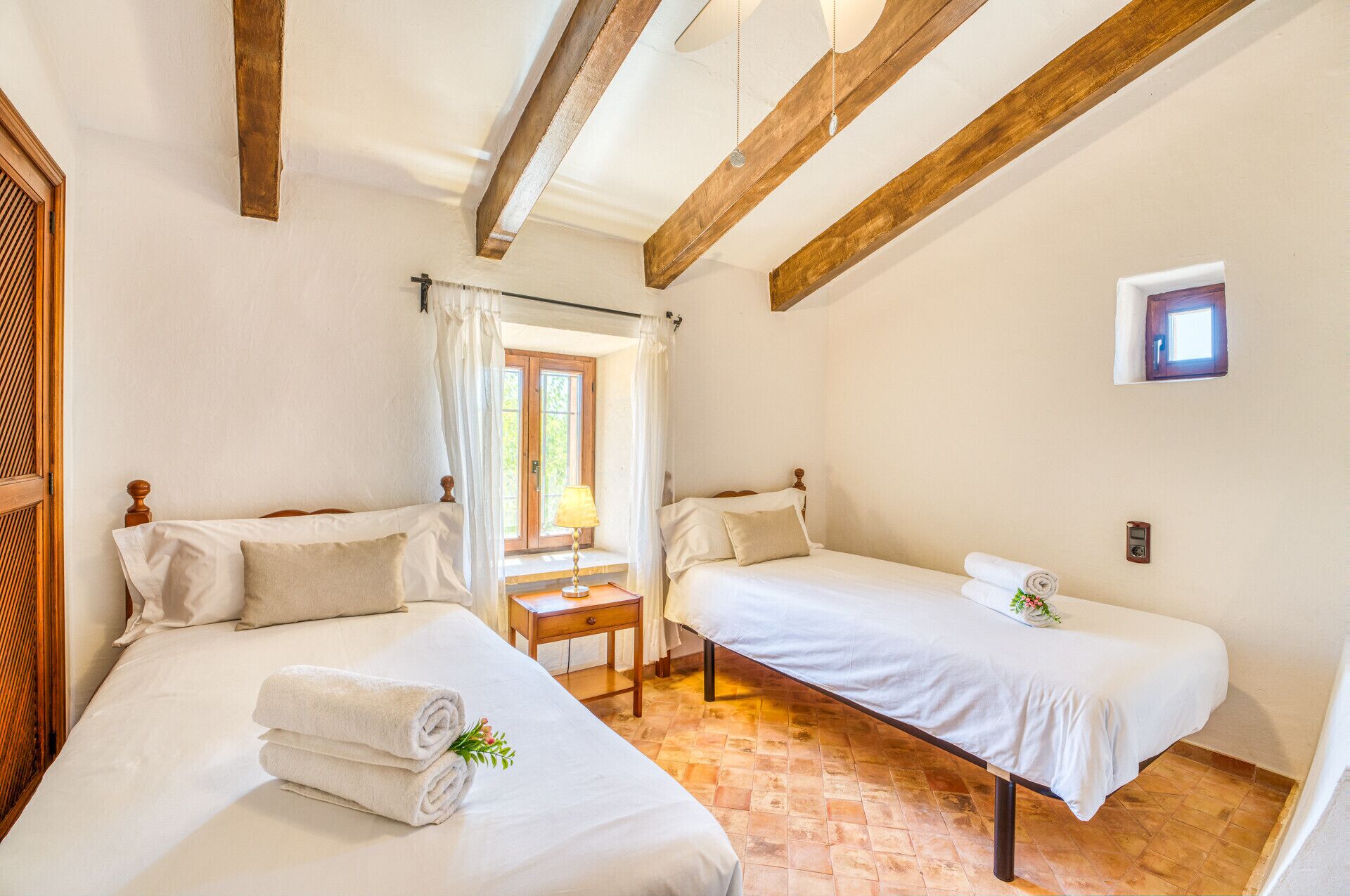 A room with two beds, a small table, and a window with curtains.