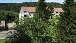 Un edificio residenziale con tetto spiovente, circondato da alberi verdi e rigogliosi e un pendio boscoso sullo sfondo.