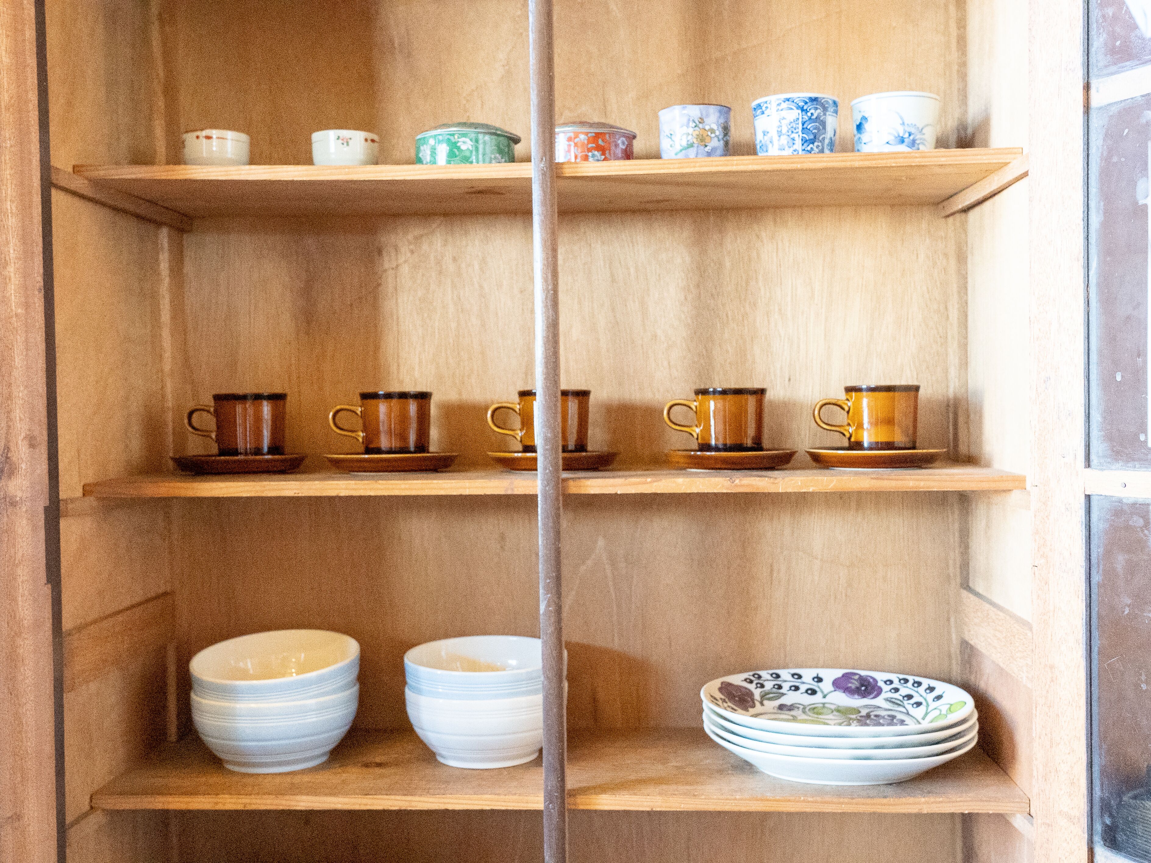 Een houten plankenrek met diverse keramische bekers en borden.