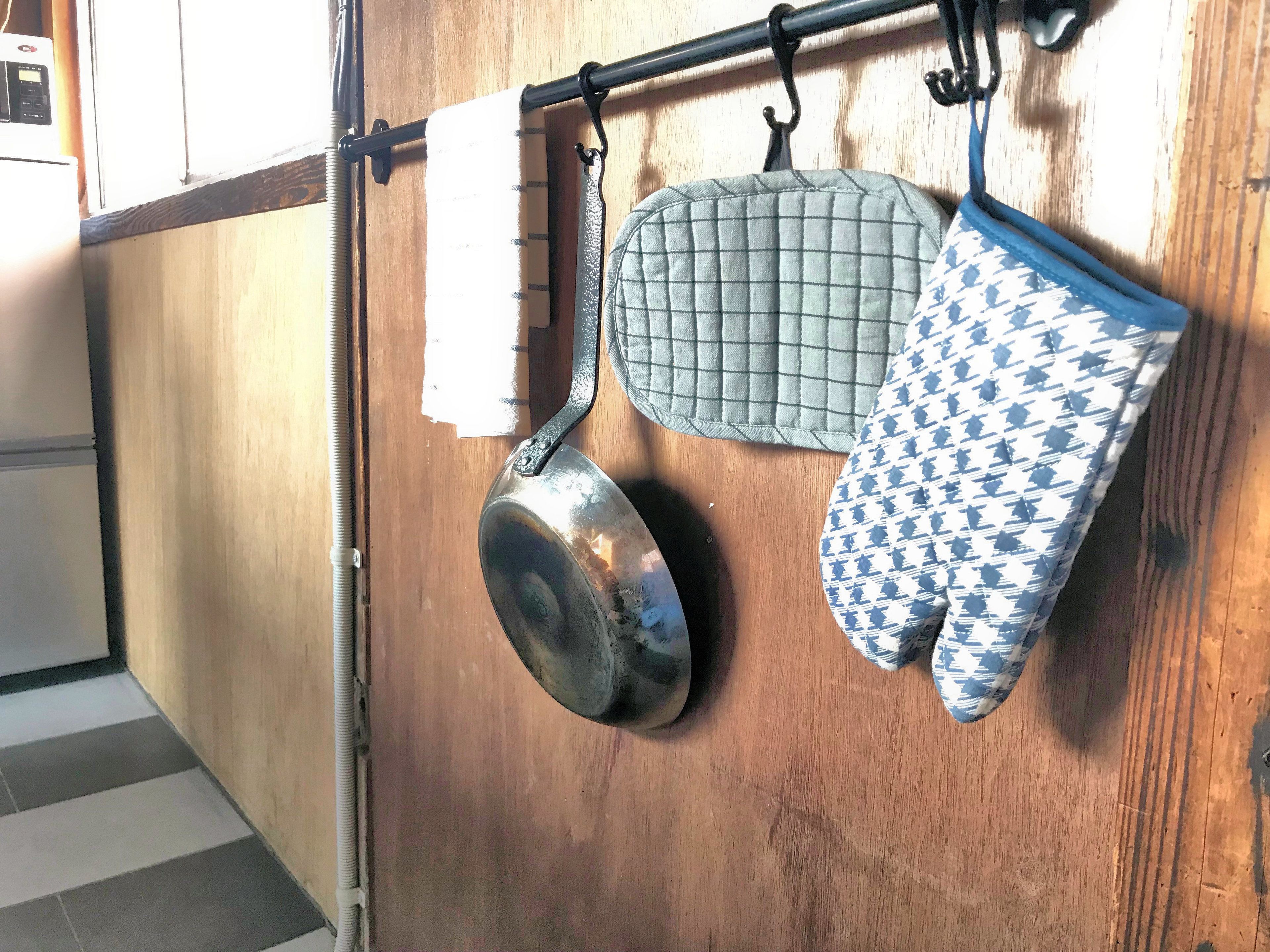 A kitchen with a wooden cabinet, a hanging pot, and oven mitts.