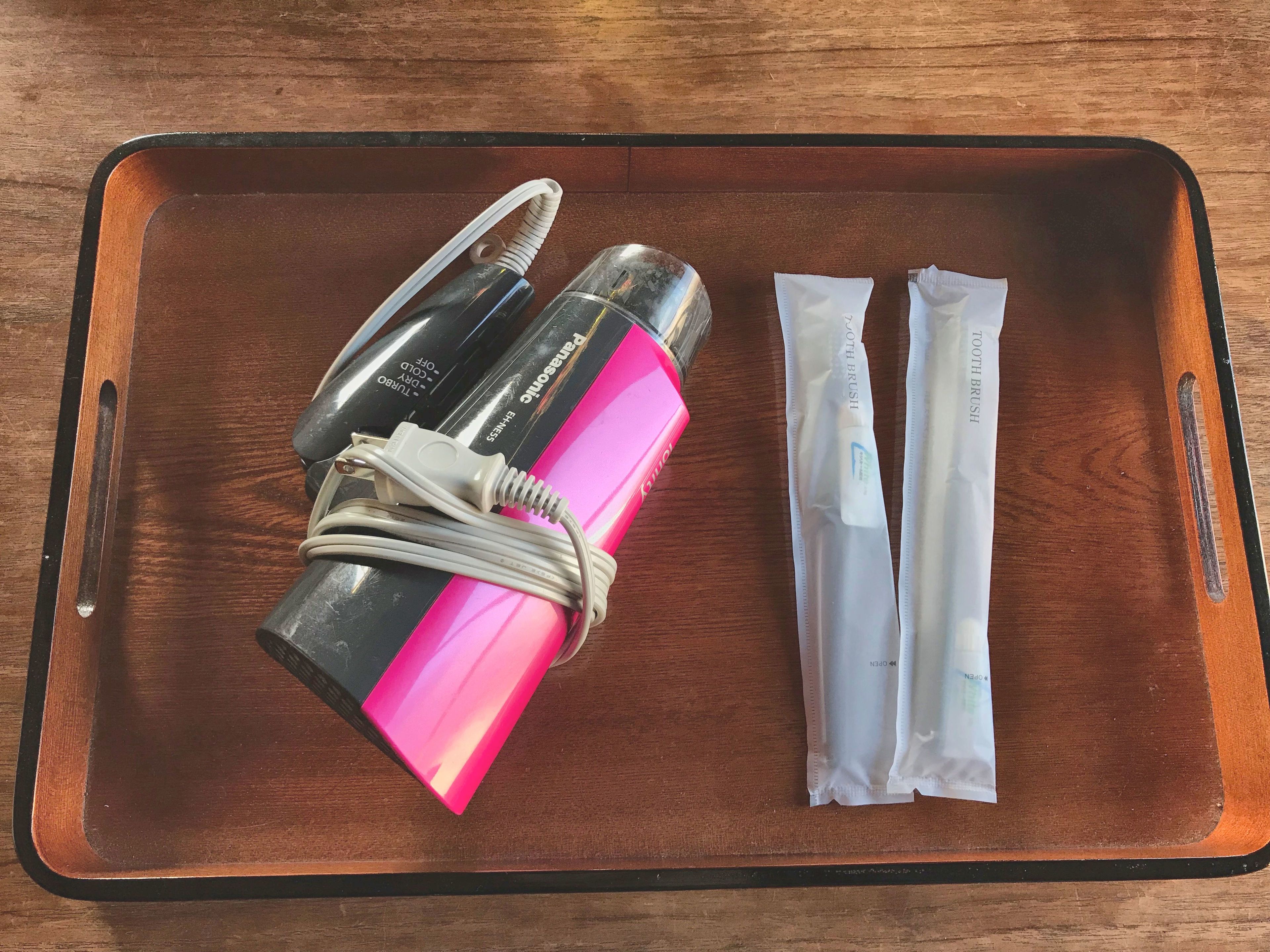 Un plateau contenant une brosse à cheveux rose et noire, un câble de chargement blanc et deux brosses à dents blanches.
