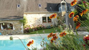 Une maison en pierre avec une piscine, entourée de fleurs et d’un jardin.