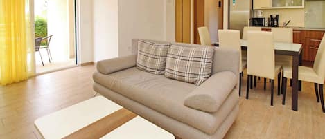 A modern living room with a sofa, a dining table, and a kitchen area.