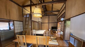 Ein traditioneller japanischer Raum mit Holzausstattung, einem Esstisch mit Stühlen, einem Bett, einem Fernseher und einer Leiter.