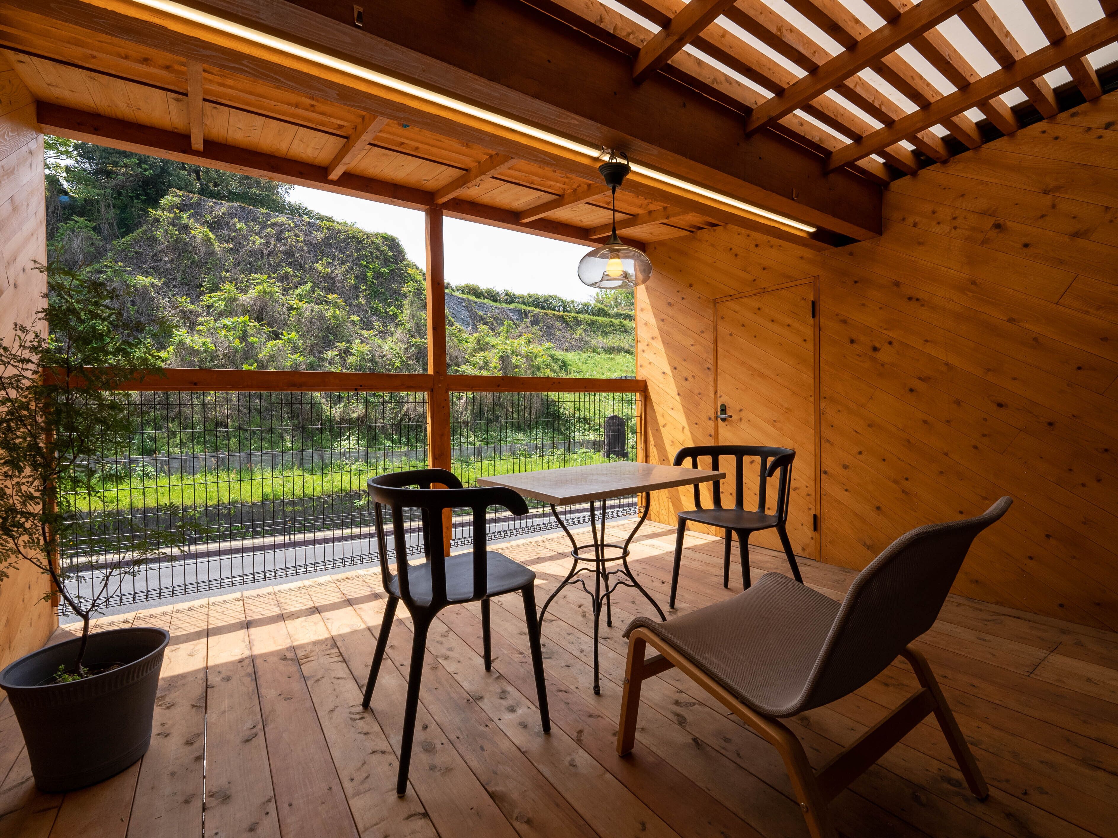 Un intérieur en bois avec une table et des chaises, de grandes fenêtres et une vue sur la verdure à l’extérieur.