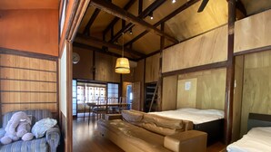 Ein gemütliches Zimmer mit Holzbalkendecke, einer Couch, einem Bett und einem Essbereich mit Stühlen und Tisch.