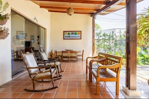 A covered patio with wooden furniture, a tiled floor, and a framed picture on the wall.