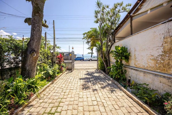 A paved pathway leading to a gated entrance with a view of the sea in the background. - Ubatuba Beachfront House - Itaguá (Ubatuba)