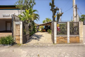A gated entrance with a paved pathway leading to a building with a sign that reads 'ESTANDE DE RESTAURANTE.' - Ubatuba Beachfront House - Itaguá (Ubatuba)