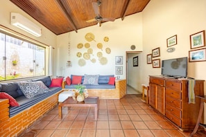 A cozy living room with a brick fireplace, a sofa with cushions, a coffee table, and a TV on a wooden cabinet. - Ubatuba Beachfront House - Itaguá (Ubatuba)