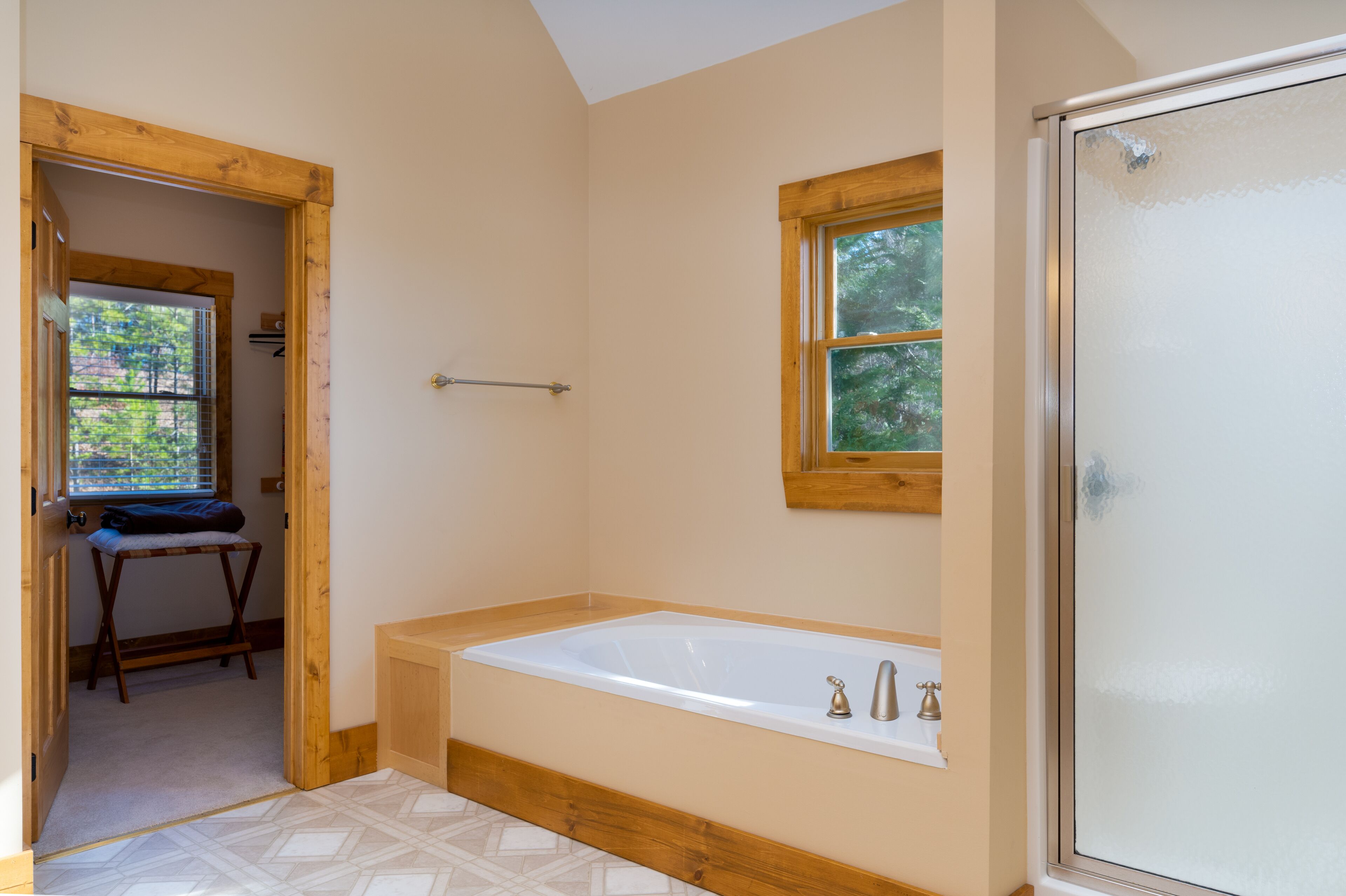 Un baño con bañera, un banco de madera y un ventanal con vistas a árboles.