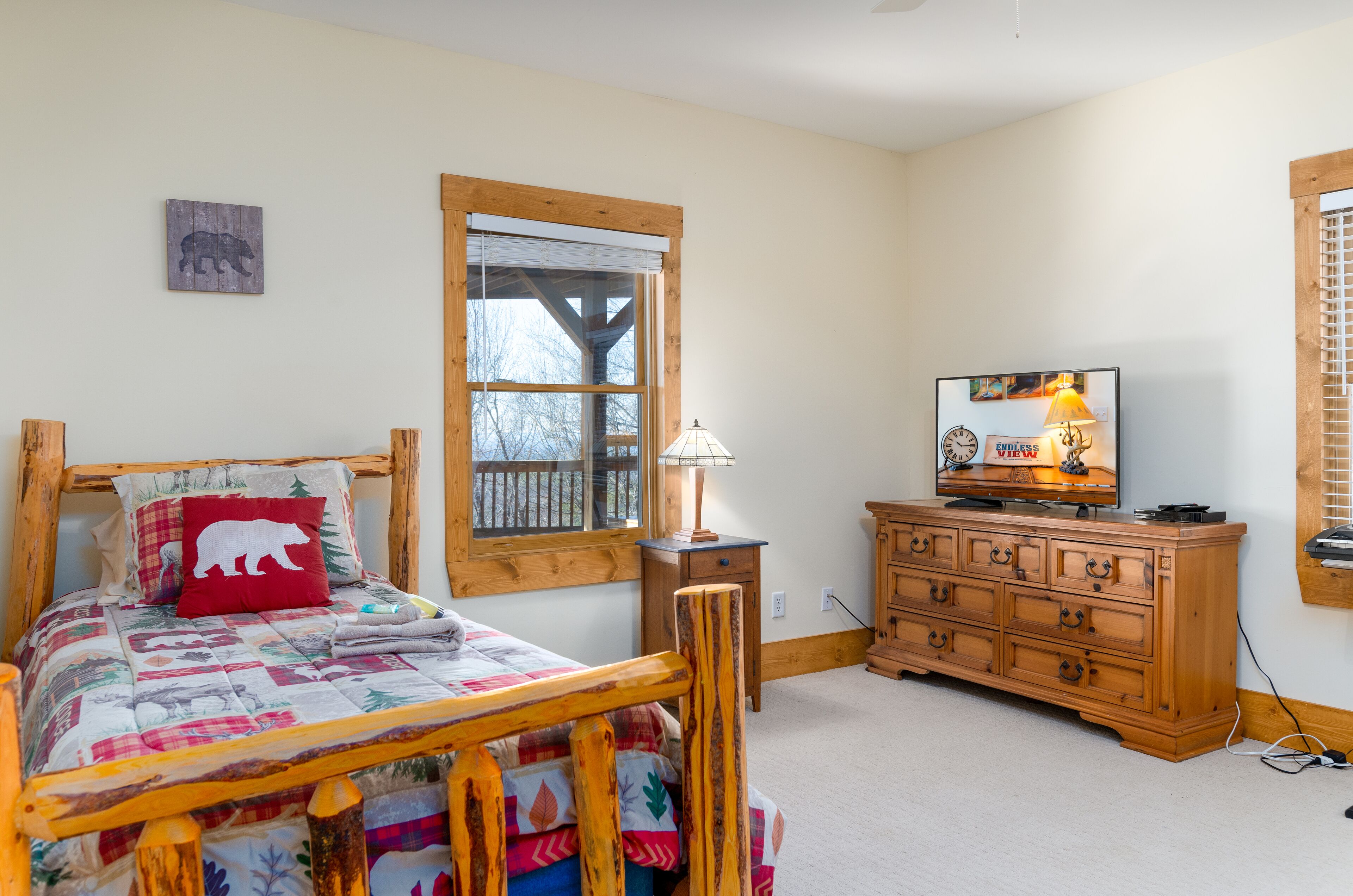 A bedroom with a wooden bed, a dresser, a television, and a window with a wooden frame.